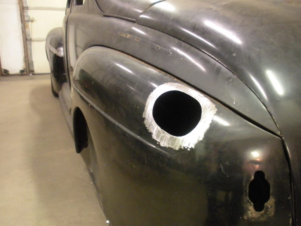Here's an alt tag for the image: Black classic car body, repair hole.