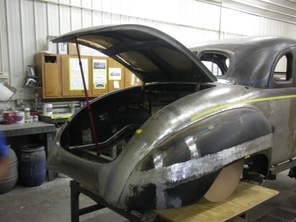 A silver car with the hood up and its doors open.