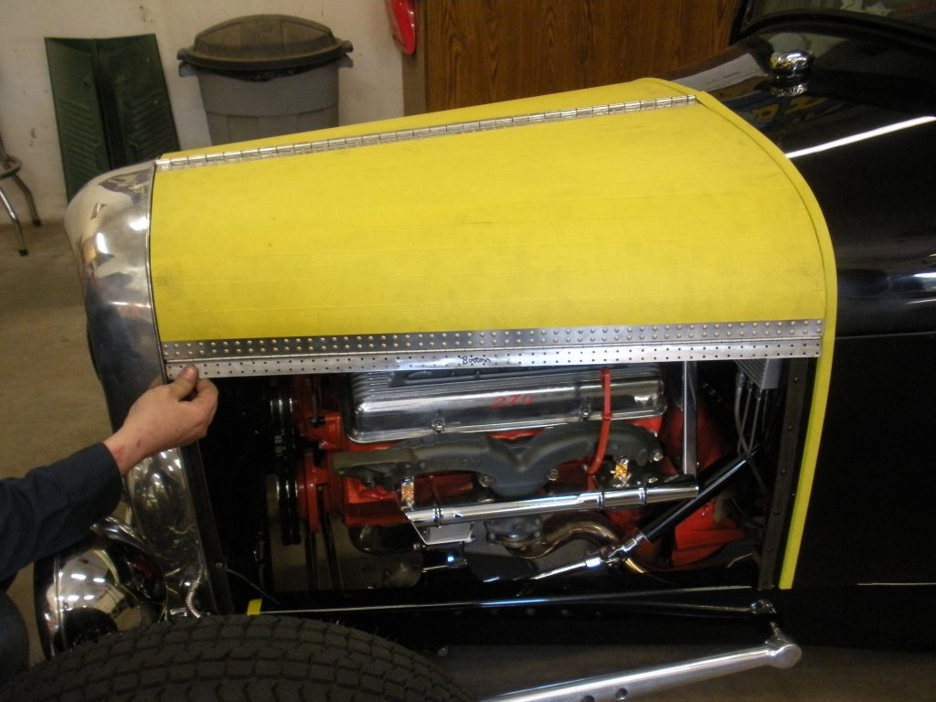 A yellow car with the hood open and tools on it.