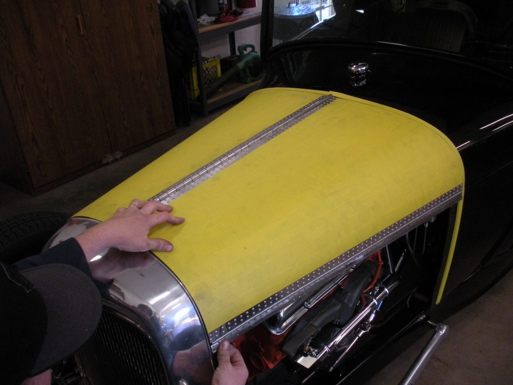 A person measuring the length of a yellow car hood.