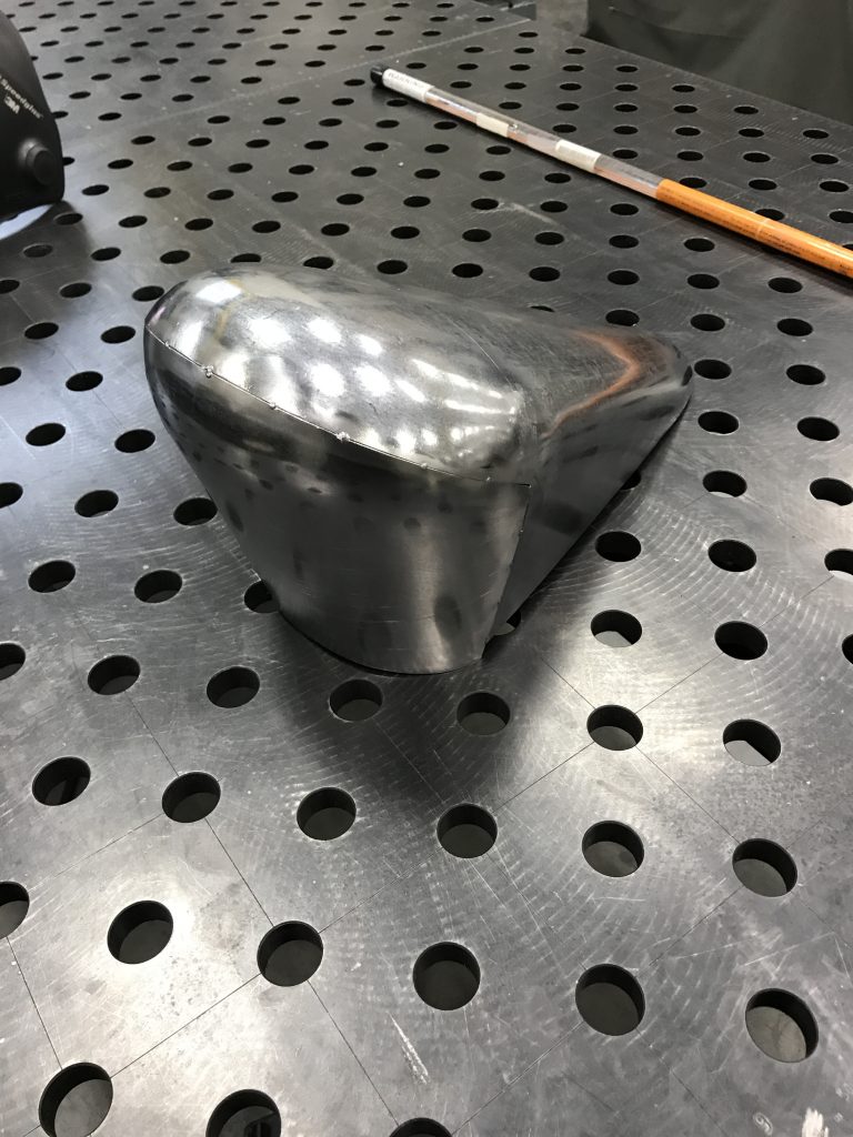Metal motorcycle seat pan on table.