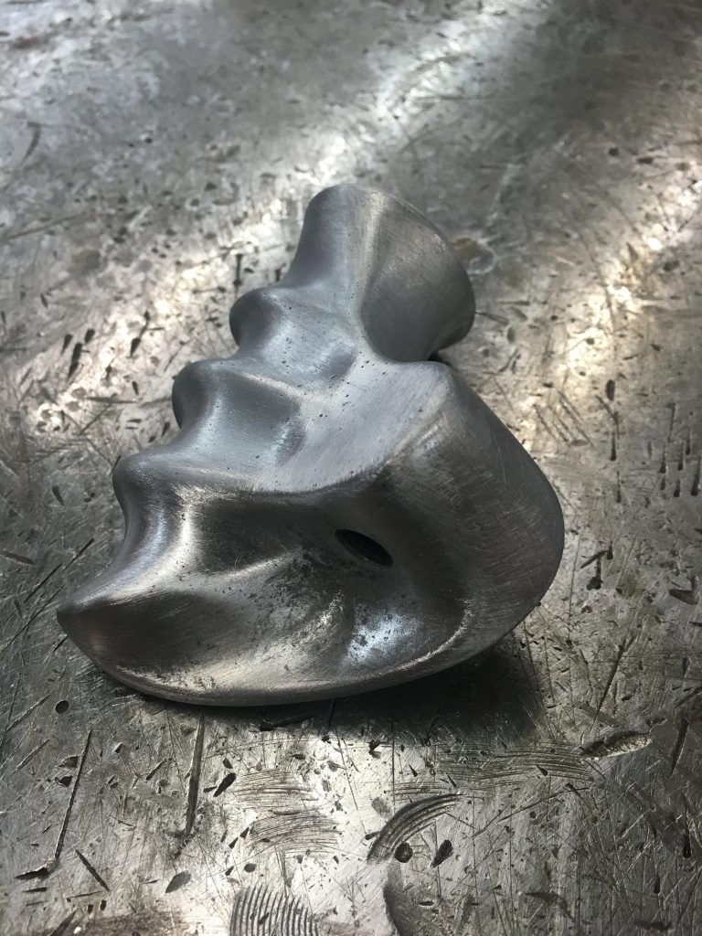 Here's an alt text suggestion: Metal climbing hold on surface.