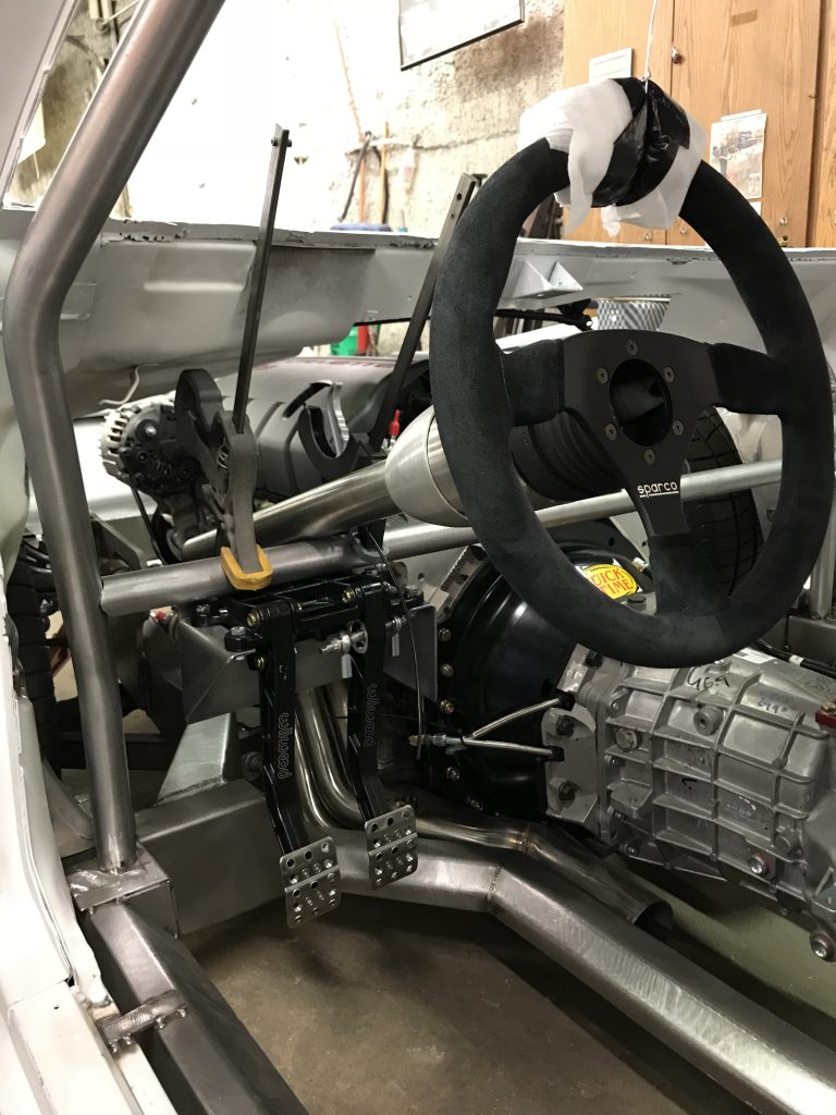 Race car interior: steering wheel, pedals, and transmission.